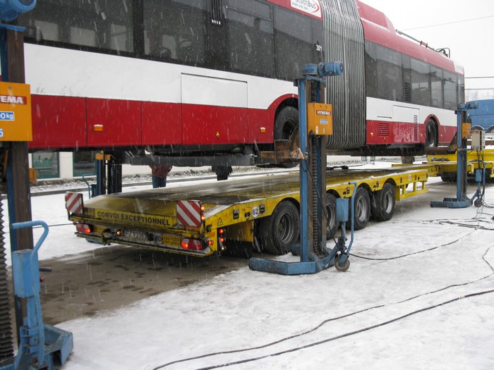 Der polnische LKW-Tieflader fährt unter dem angehobenen Gelenkobus heraus.
